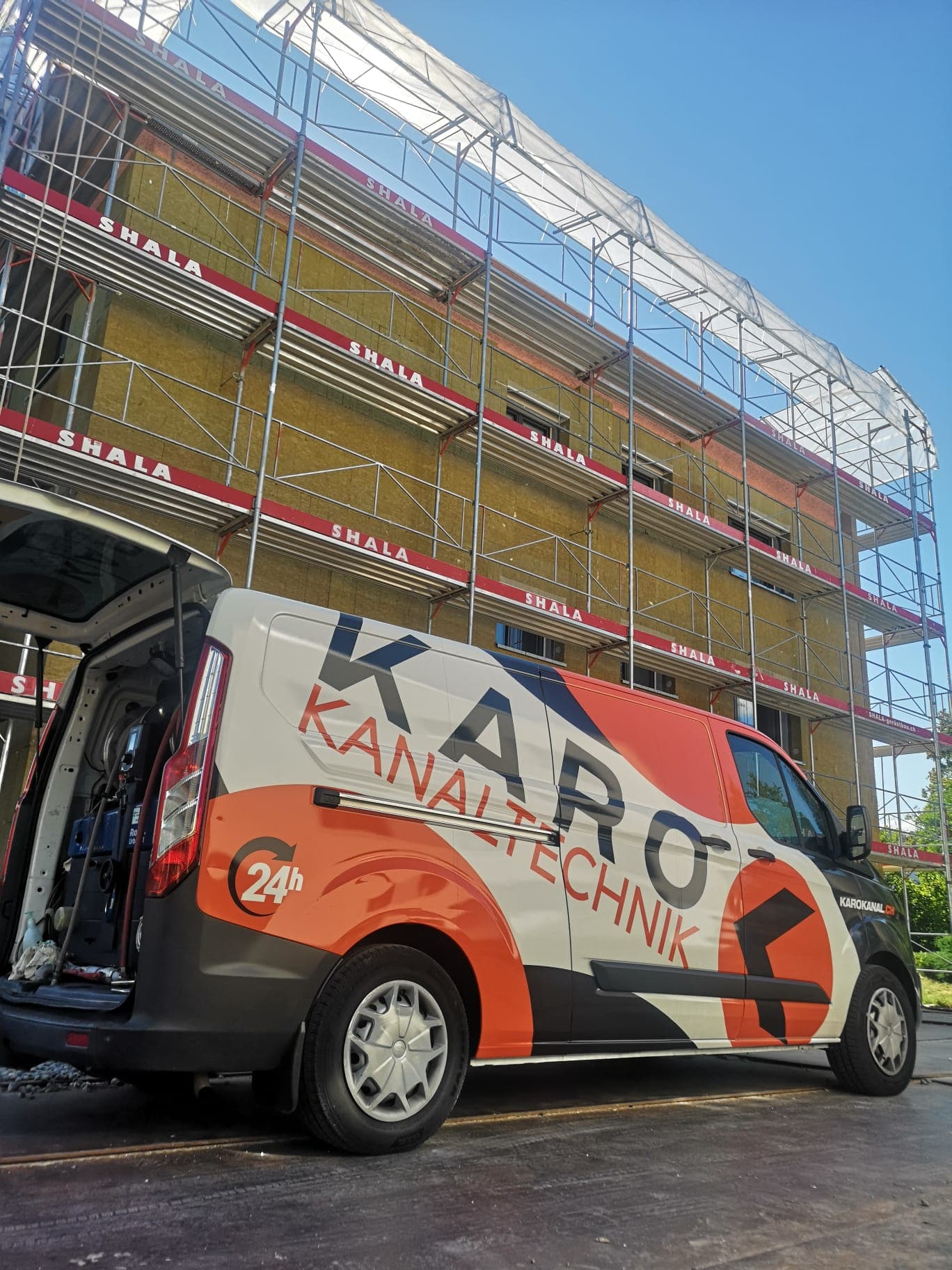 Kanalarbeiten an einem eingerüsteten Neubau, Einsatzfahrzeug mit offener Heckklappe